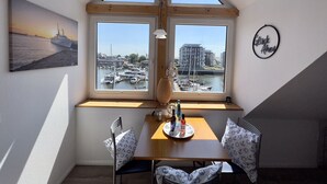 Een eethoek met een tafel, stoelen en uitzicht op een jachthaven door grote ramen.