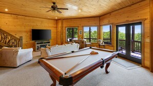 A wooden interior with a pool table, sofas, a television, and large windows offering a view of greenery. - Cascading View Lodge♡ Mtn Views, hot tub, fire pit, < 20 min from Blue Ridge (Blue Ridge)