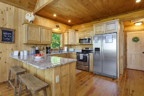 Cocina de cabaña de madera con encimeras de granito, electrodomésticos de acero inoxidable y un letrero de bienvenida.
