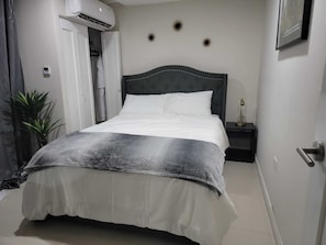A neatly made bed with a grey and white duvet, a dark headboard, and a bedside table with a lamp.