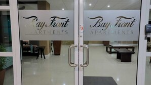A glass door entrance to Bay Front Apartments with a sign, metal handles, and a tiled floor. - Bayfront Villas and Apt (Portmore)