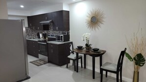A modern kitchen with dark cabinetry, a microwave, and a dining area with a table and chairs. - Bayfront Villas and Apt (Portmore)