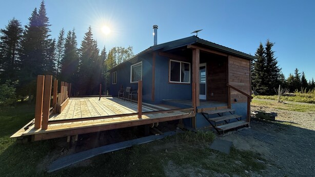 Uma cabana pequena com deck de madeira, chaminé e painel solar.