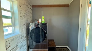 Uma lavanderia com uma máquina de lavar, uma mesa pequena e uma porta.