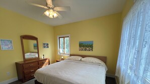Ett sovrum med en säng, en byrå, en spegel, ett fönster och en takfläkt.
