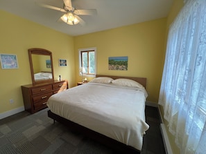 Une chambre à coucher comprenant un lit, une commode, un miroir, une fenêtre et un ventilateur de plafond.
