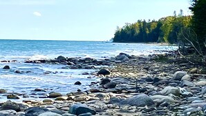 En stenig kustlinje med utsikt över havet och en skogbeklädd ö i fjärran.
