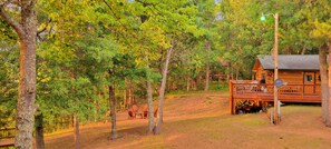 Un chalet rustique doté d’une terrasse et d’un espace salon extérieur, le tout entouré d’arbres.