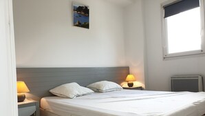 Een netjes opgemaakt bed met twee kussens, een nachtkastje met een lamp en een foto aan de muur.