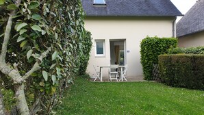 Een huis met een witte gevel, een deur en een raam. In de voortuin staan een tafel en stoelen.