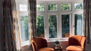 A room with a large window, two chairs, a small table, and a bed.