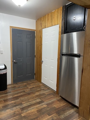Compact kitchen with a stainless steel refrigerator, double door oven, and microwave, complemented by wooden paneling and herringbone-patterned flooring.