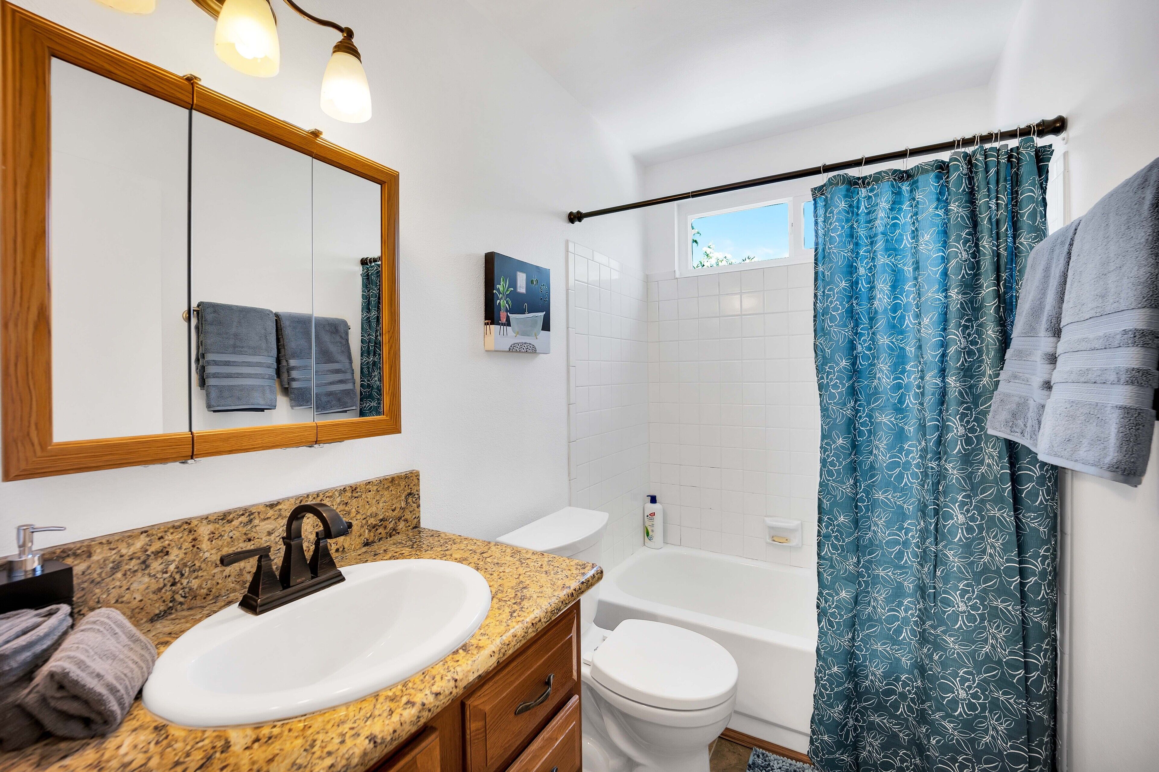 A bathroom with a granite countertop sink, a white toilet, a bathtub, and a shower curtain.