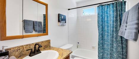 A bathroom with a granite countertop sink, a white toilet, a bathtub, and a shower curtain.