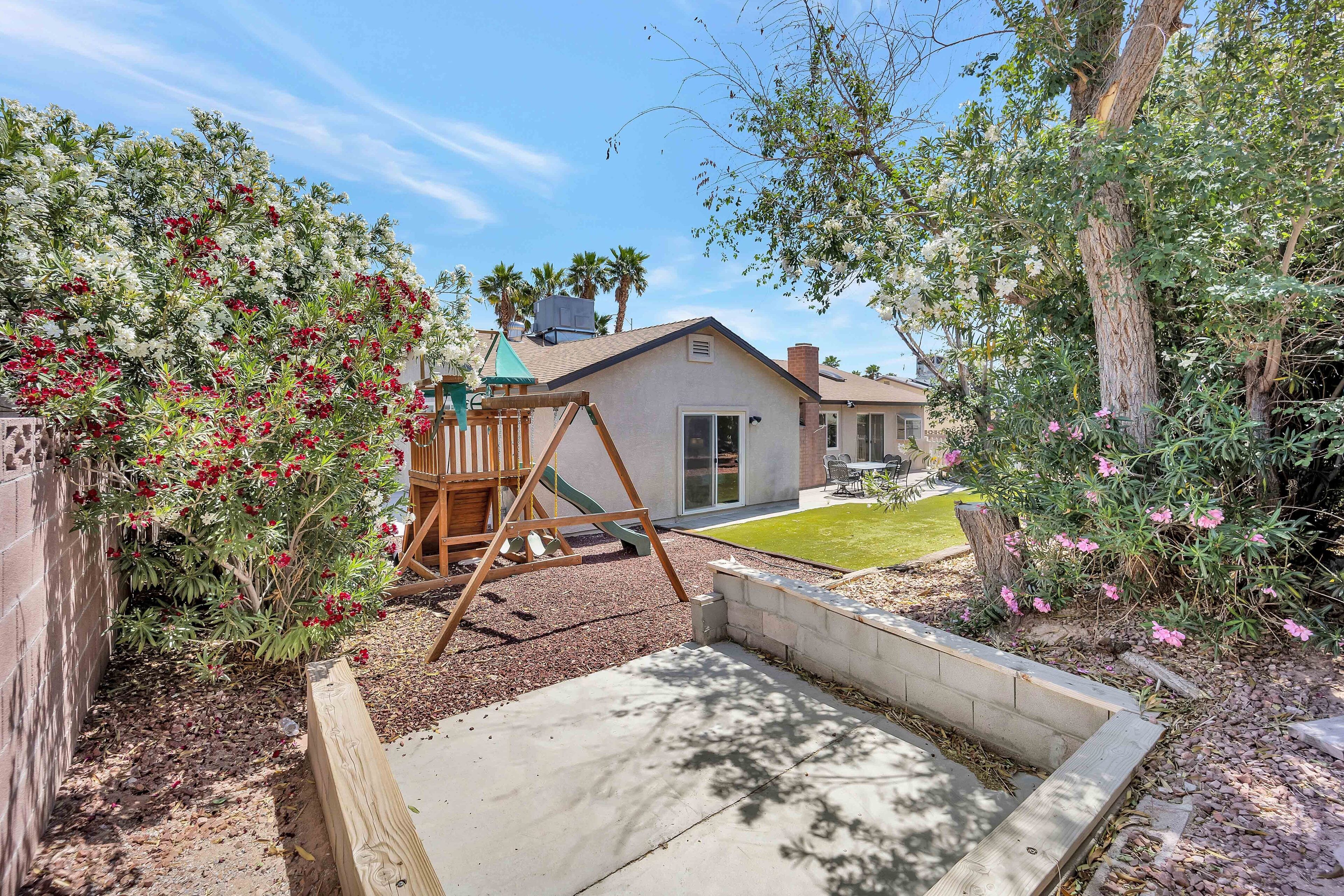 A backyard with a wooden swing set, a concrete play area, and a house in the background.