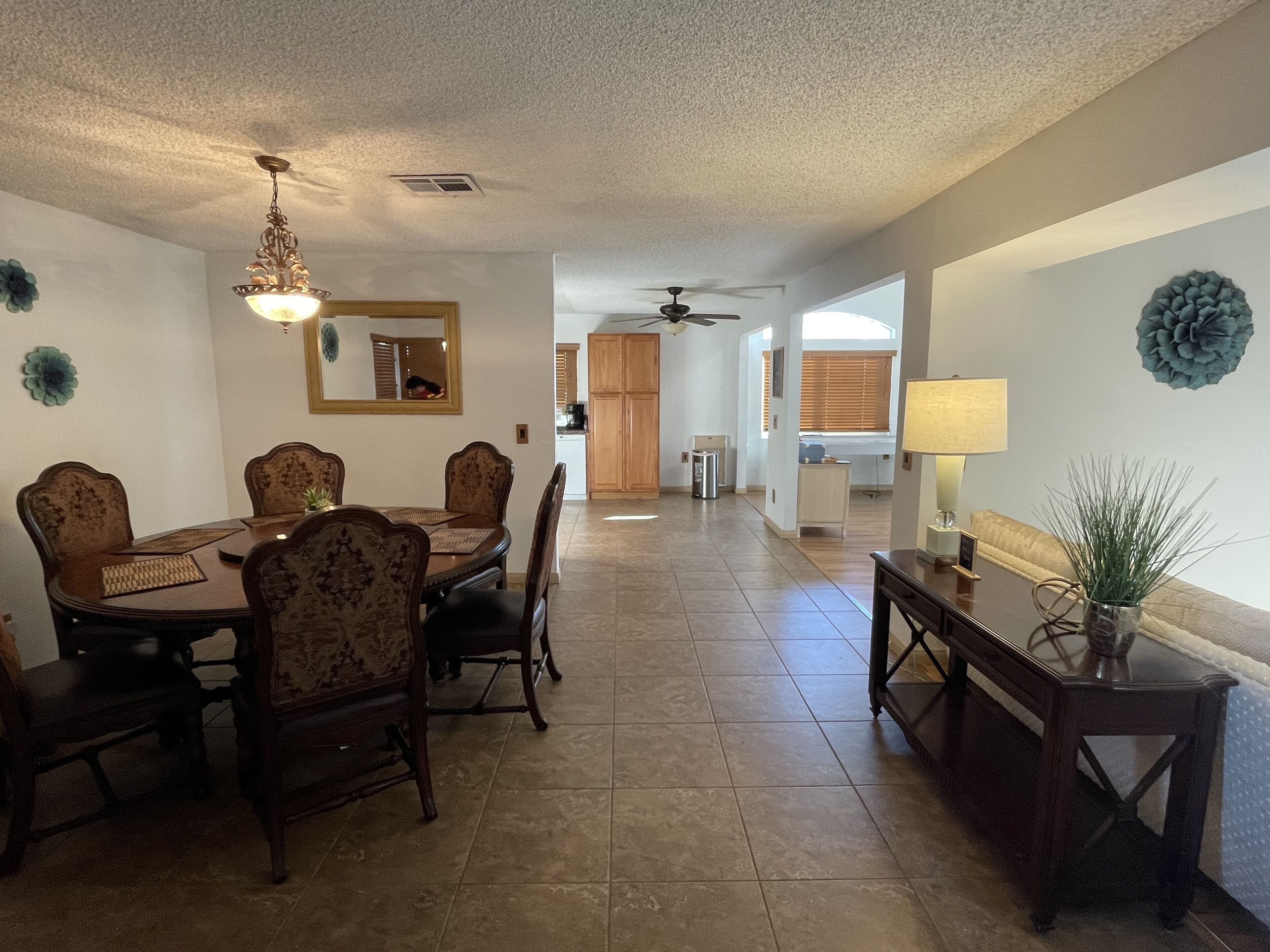 A dining area with a wooden table and chairs, a ceiling fan, and a view into the kitchen.