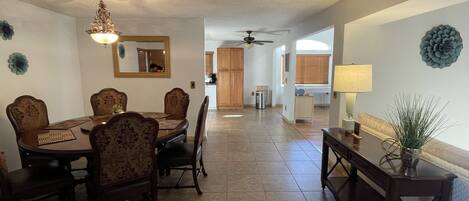 A dining area with a wooden table and chairs, a ceiling fan, and a view into the kitchen.