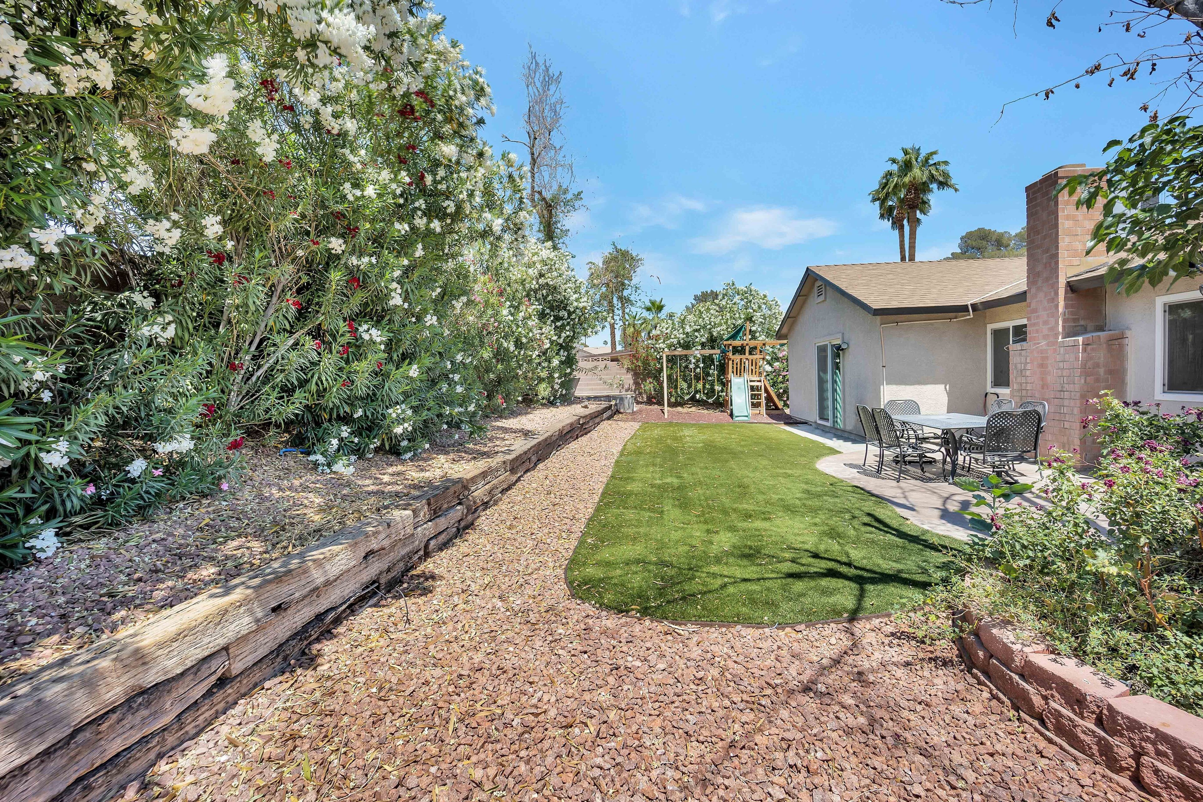A backyard with a patio, a lawn, and a variety of plants and trees.