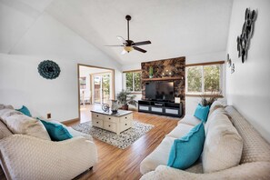 A spacious living room with a ceiling fan, a fireplace, and a large TV.