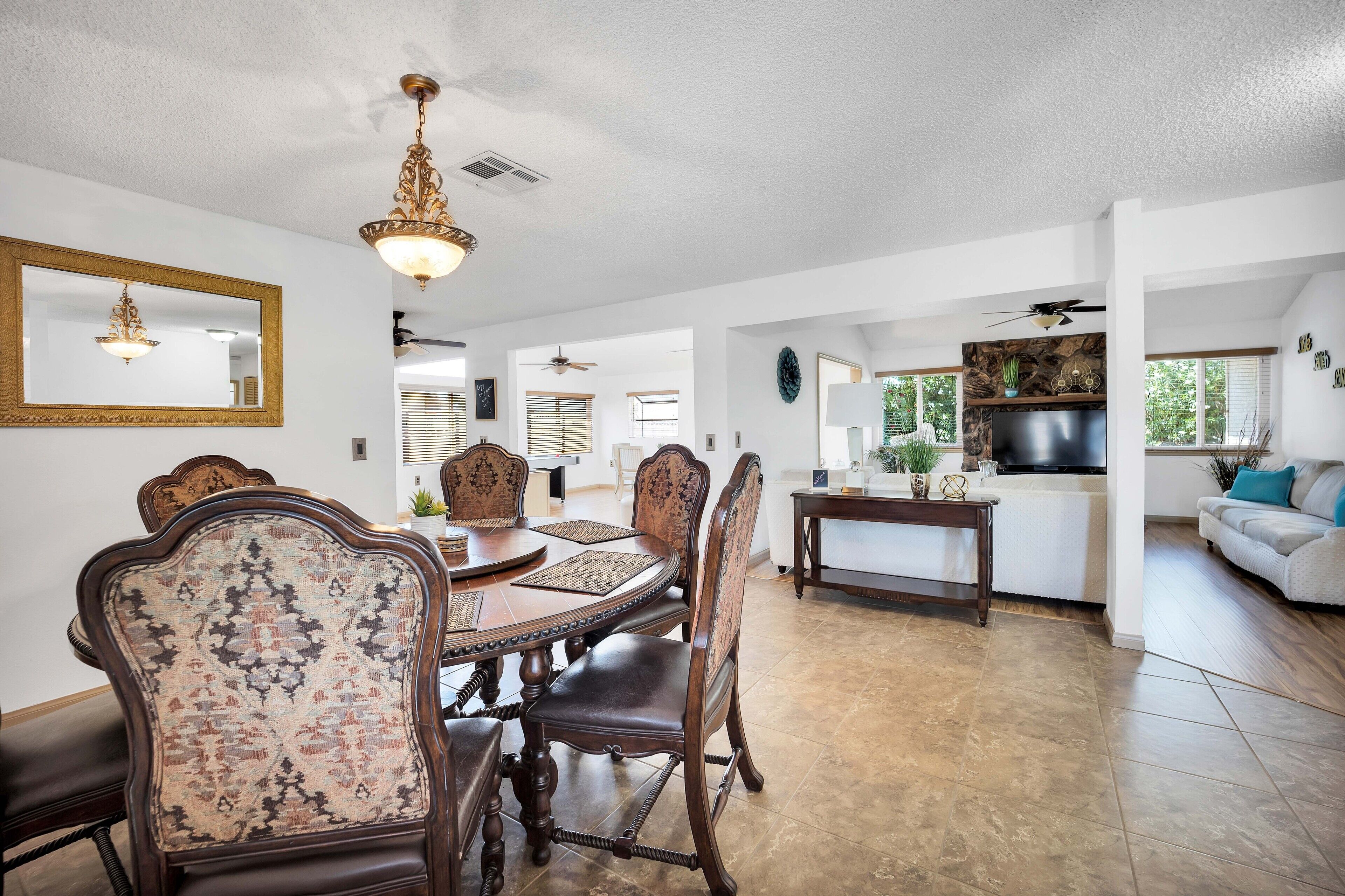A spacious dining area with a large wooden table and ornate chairs, a kitchen with a modern stove, and a living area with a sofa and decorative plants.