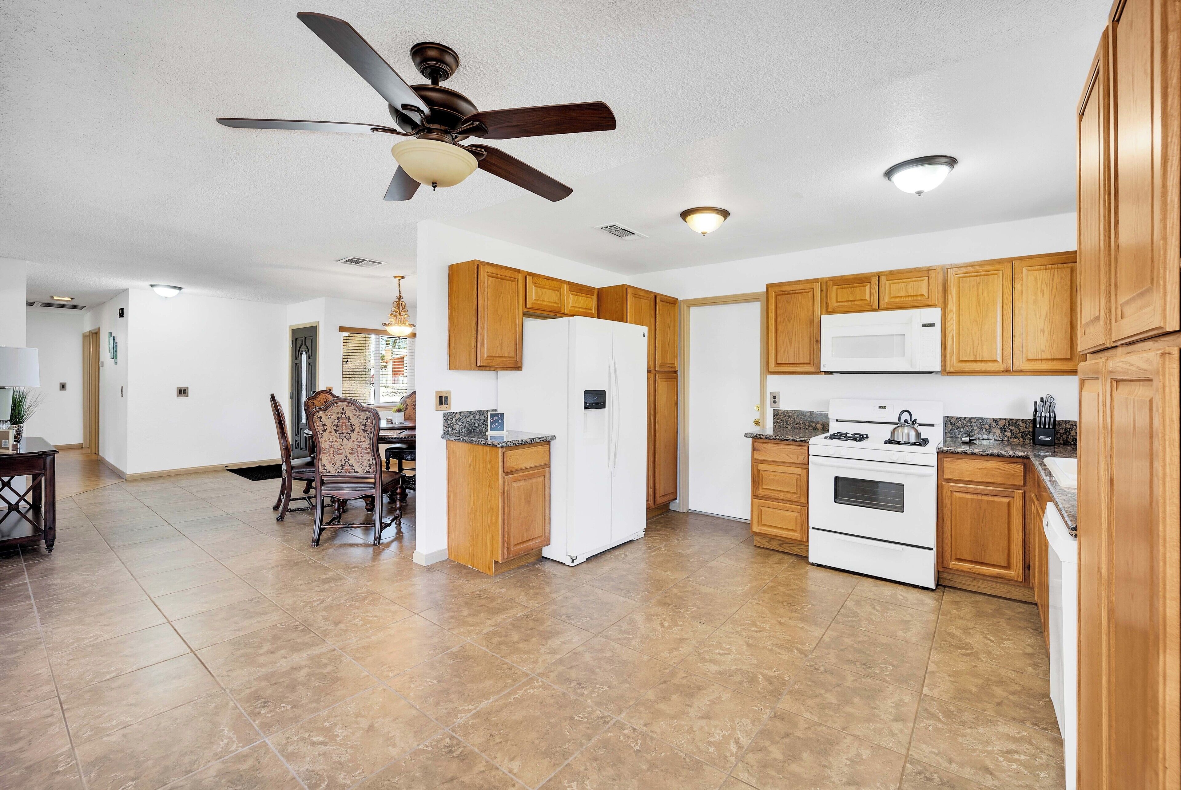 A modern kitchen with wooden cabinets, a white refrigerator, a stove, and a ceiling fan.