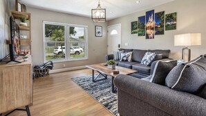 Een moderne woonkamer met een grijze bank, een salontafel en een groot raam met uitzicht op geparkeerde auto's.