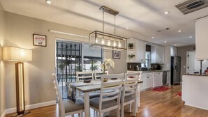 Een moderne keuken met witte kasten, een centraal eiland en een eethoek met een tafel en stoelen.