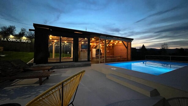A modern house with a swimming pool, outdoor seating, and a well-lit interior.