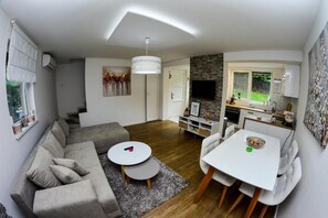A modern living room with a grey sofa, a round coffee table, and a dining area with a white table and chairs.