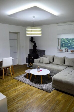 A modern living room with a sofa, a round coffee table, a fireplace, and a window with a view of greenery.