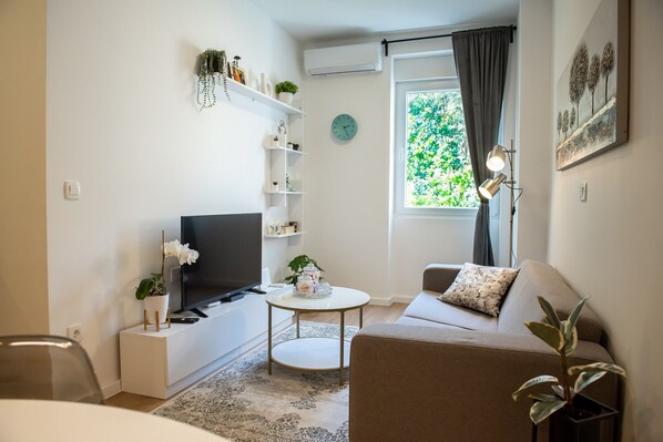 A modern living room with a flat-screen TV, a sofa, a coffee table, and a small side table.
