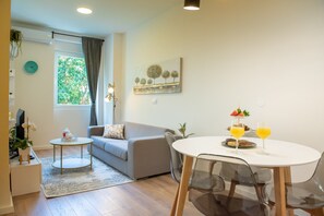 A modern living room with a sofa, a coffee table, and a dining table set for two with drinks.