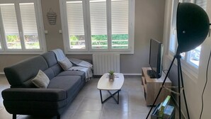A living room with a grey sofa, a white coffee table, a TV on a wooden stand, and a tripod with a light. - Ideal Holiday Home for the 2024 Olympics Games in Marseille: Comfort & Proximity (Marseille)