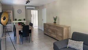 A living room with a grey sofa, a wooden dining table with chairs, a wooden cabinet, and a floor lamp. - Ideal Holiday Home for the 2024 Olympics Games in Marseille: Comfort & Proximity (Marseille)