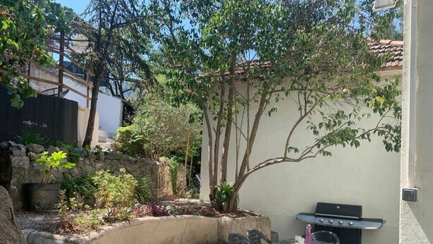 An outdoor patio with a round table and chairs, a grill, and a stone planter with plants. - Ideal Holiday Home for the 2024 Olympics Games in Marseille: Comfort & Proximity (Marseille)