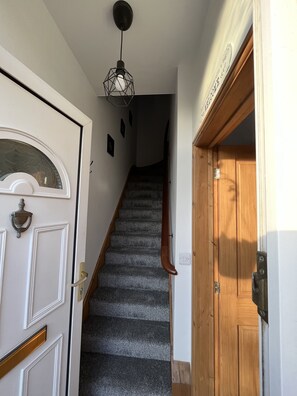 A staircase with a wooden handrail, a white door with a glass panel, and a wall-mounted light fixture.