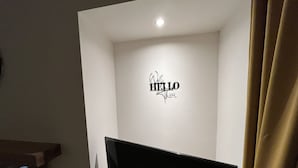 A room with a flat-screen TV mounted on the wall, a white ceiling, and a 'HELLO' sign above the TV.