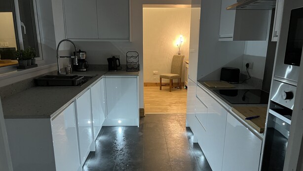 A modern kitchen with white cabinets, a black tiled floor, and a wooden dining area.