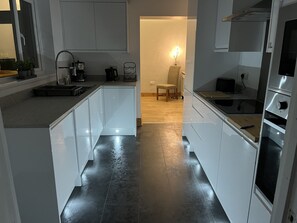 A modern kitchen with white cabinets, a black tiled floor, and a wooden dining area.