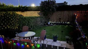 A patio with a round table and chairs, surrounded by a wooden fence and a hedge.