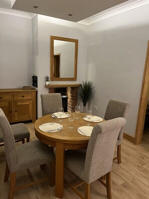 Un coin repas comprenant une table ronde en bois, six chaises grises à revêtement rembourré et un grand miroir placé au-dessus de la table.