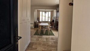A hallway with a black door, white walls, and a tiled floor leading to a dining area with a table and chairs. - Renovated house with garden - 3 min walk from Le Bureau and Nauzan beaches (Saint-Palais-sur-Mer)
