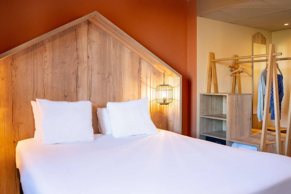 A hotel room with a large bed, wooden headboard, and a wooden wardrobe.