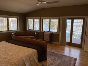 Ein Schlafzimmer mit einem großen Bett, einem Sessel, einem Heizkörper und Blick auf eine verschneite Landschaft durch die Fenster.