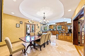 Ein geräumiger Essbereich mit einem großen Tisch und Stühlen, einer Chandelier und einer Küche mit Holzschränken und einer großen Kochinsel.