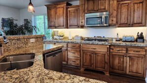 A kitchen with granite countertops, wooden cabinets, a built-in microwave, and a dishwasher.