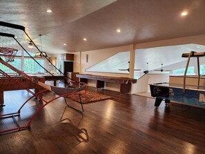 Un grand espace intérieur doté d’un plancher en bois, d’un panier de basket, d’un trampoline et d’une table de billard.