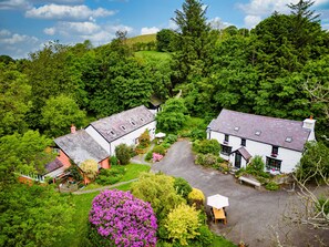 Escape to a serene cottage surrounded by lush gardens and mature trees, featuring a spacious patio for relaxation.