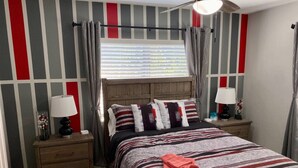 A bedroom with a bed, two nightstands, a window with curtains, a wooden headboard, and a ceiling fan.