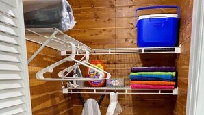 A laundry room with a drying rack, iron, basket, and storage shelves.